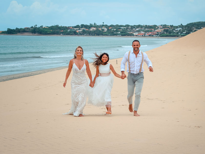 Casal de noivos e filha correndo na praia